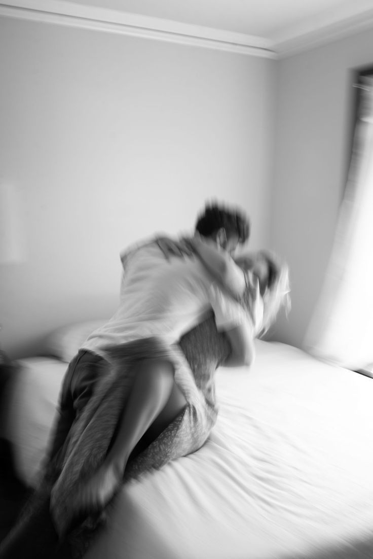 black and white photograph of two people hugging on a bed in a room with light coming through the window