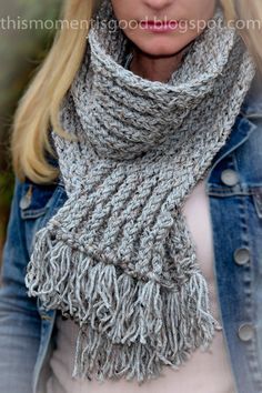 a woman wearing a gray knitted scarf with fringes on the ends and a denim jacket over her shoulders