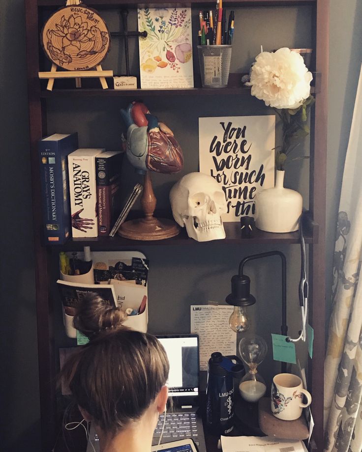 a woman sitting at a desk with a laptop computer in front of her and bookshelf behind her