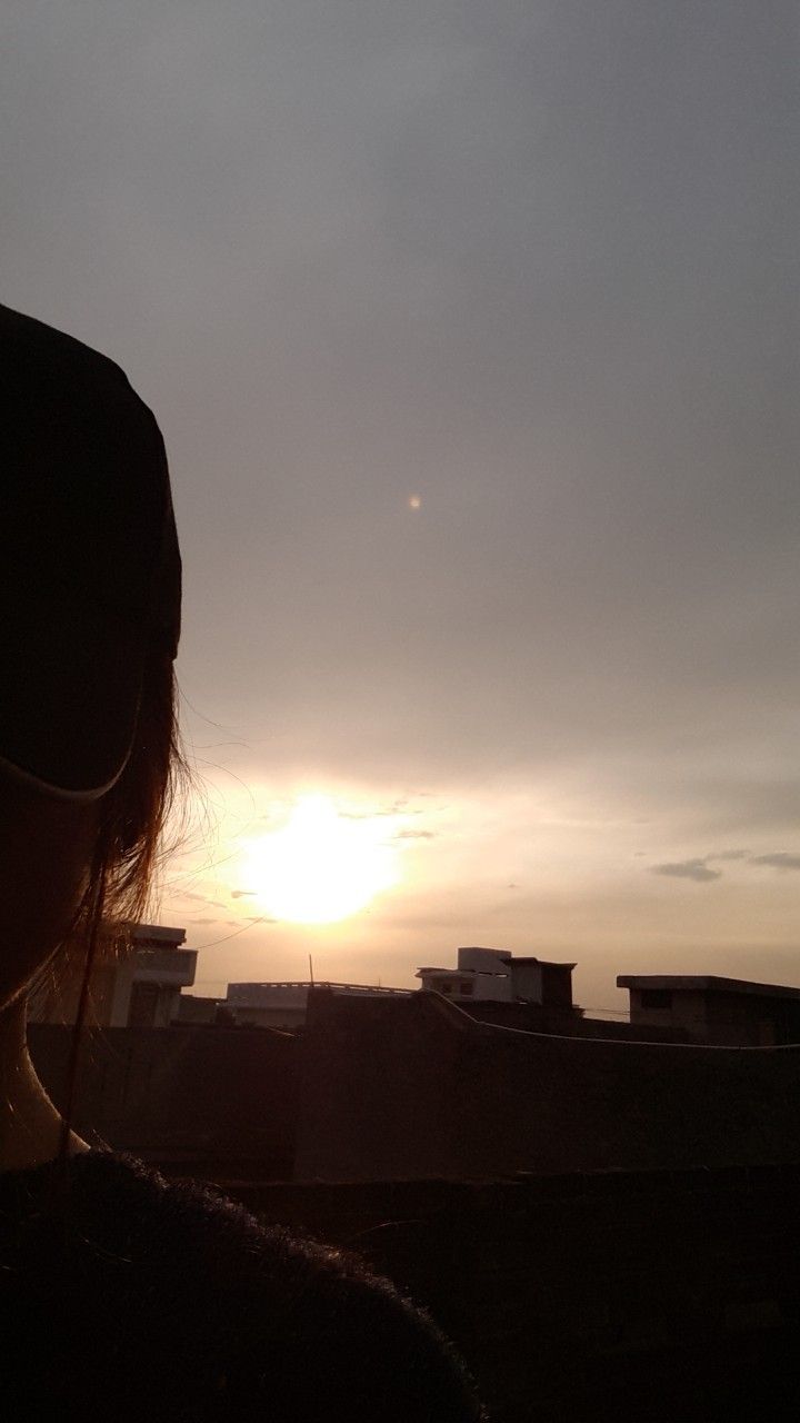 the sun is setting behind a woman with sunglasses on her head and buildings in the background