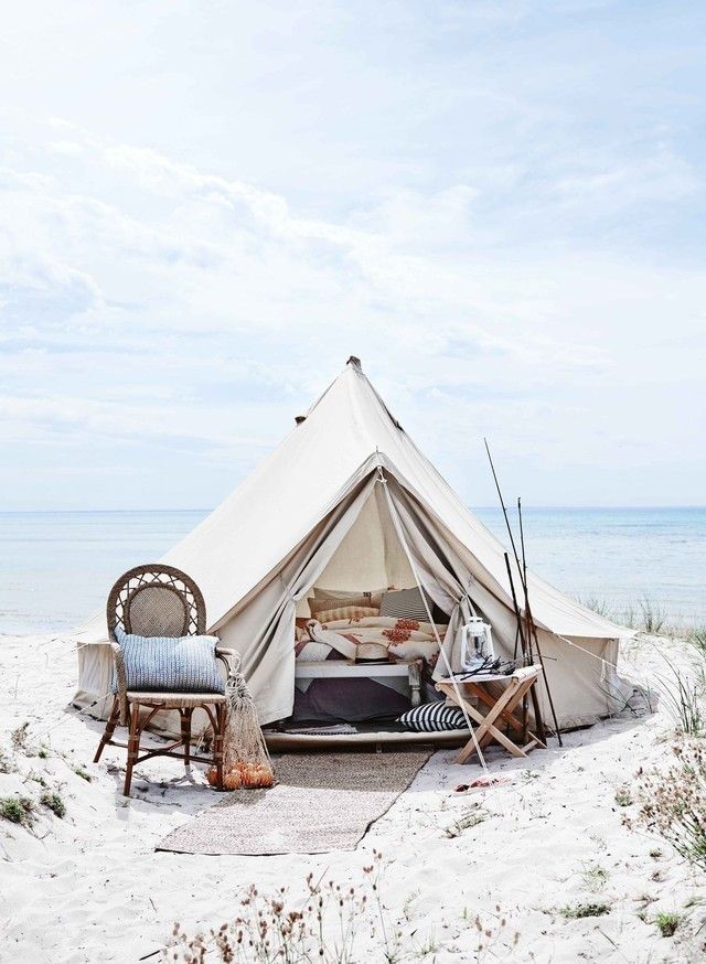 a tent set up on the beach with two chairs and a bed in front of it