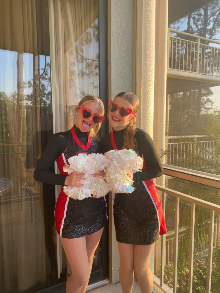 two young women in cheerleader outfits standing next to each other near a window with the sun shining on them