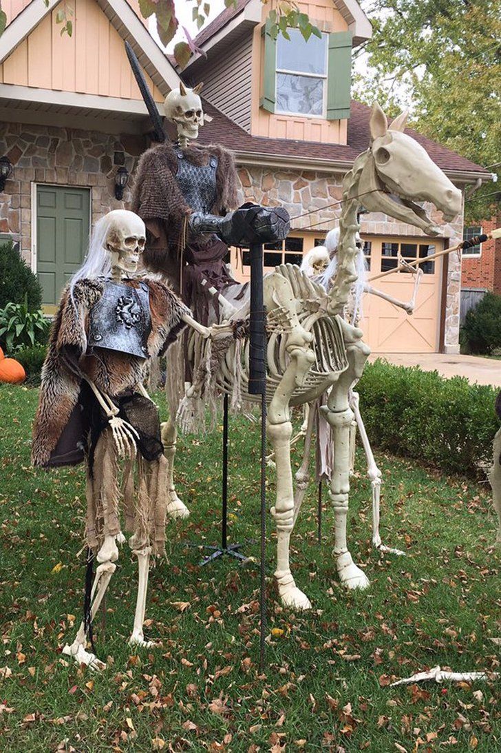 skeleton statues in front of a house decorated for halloween with skeletons on the lawn and horses