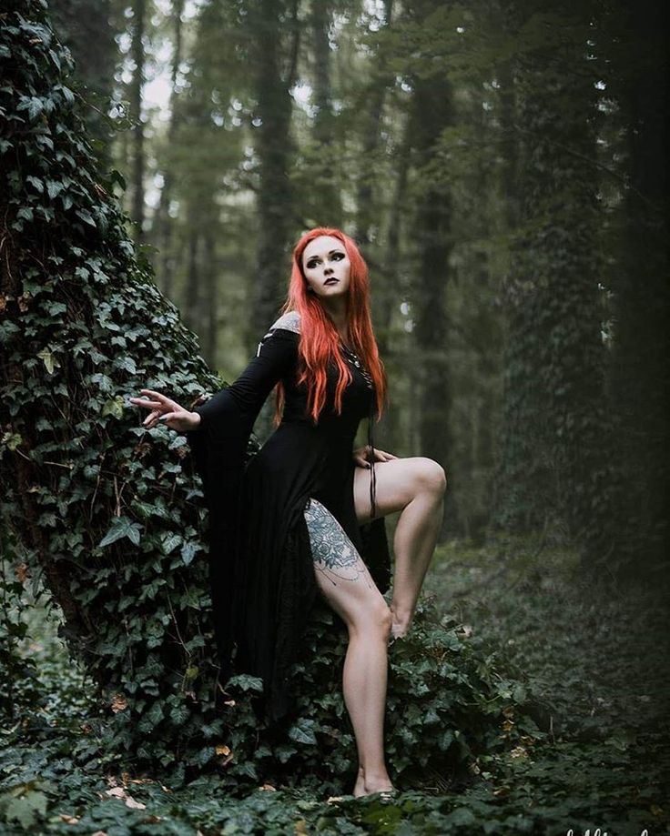 a woman with red hair and makeup is posing in the woods wearing a black dress