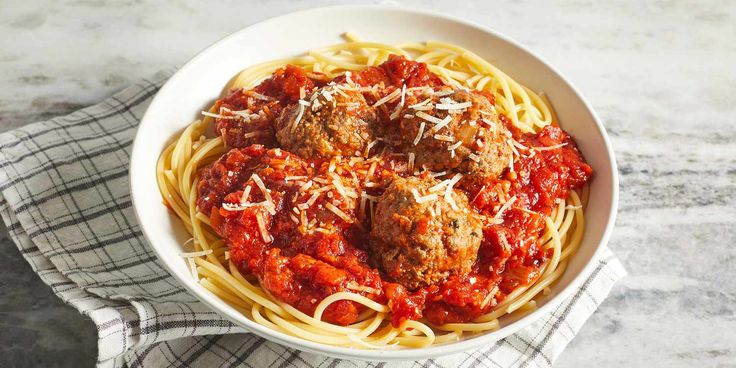 a white bowl filled with spaghetti and meatballs on top of a table next to a napkin