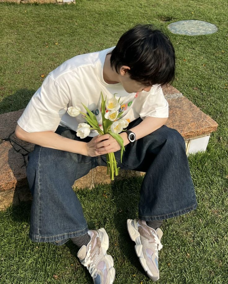 a boy sitting on a bench with flowers in his lap and looking down at the ground