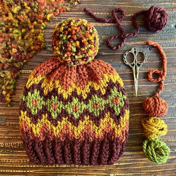 a knitted hat sitting on top of a wooden table next to scissors and yarn