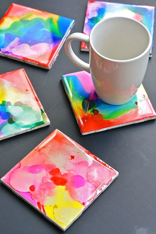 four square coasters with colorful paint on them and a coffee cup in the middle