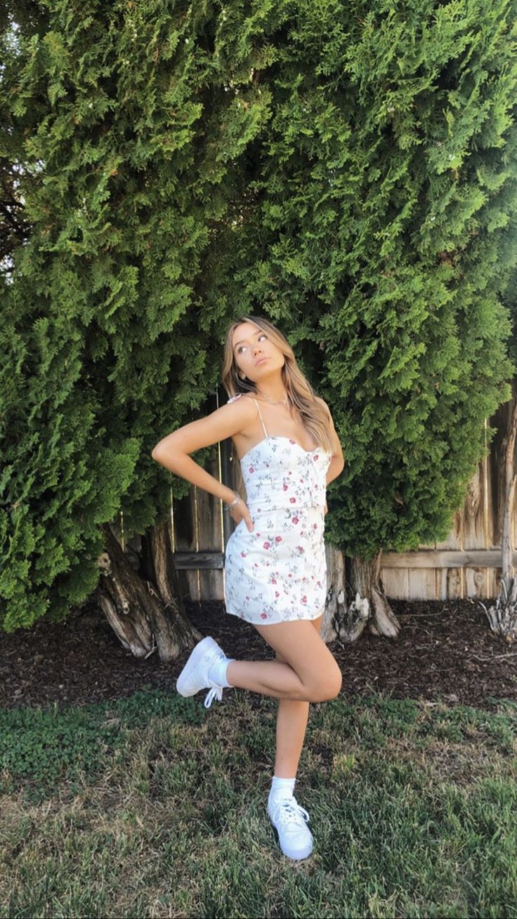 a woman posing in front of a tree with her hands on her hips and wearing white tennis shoes