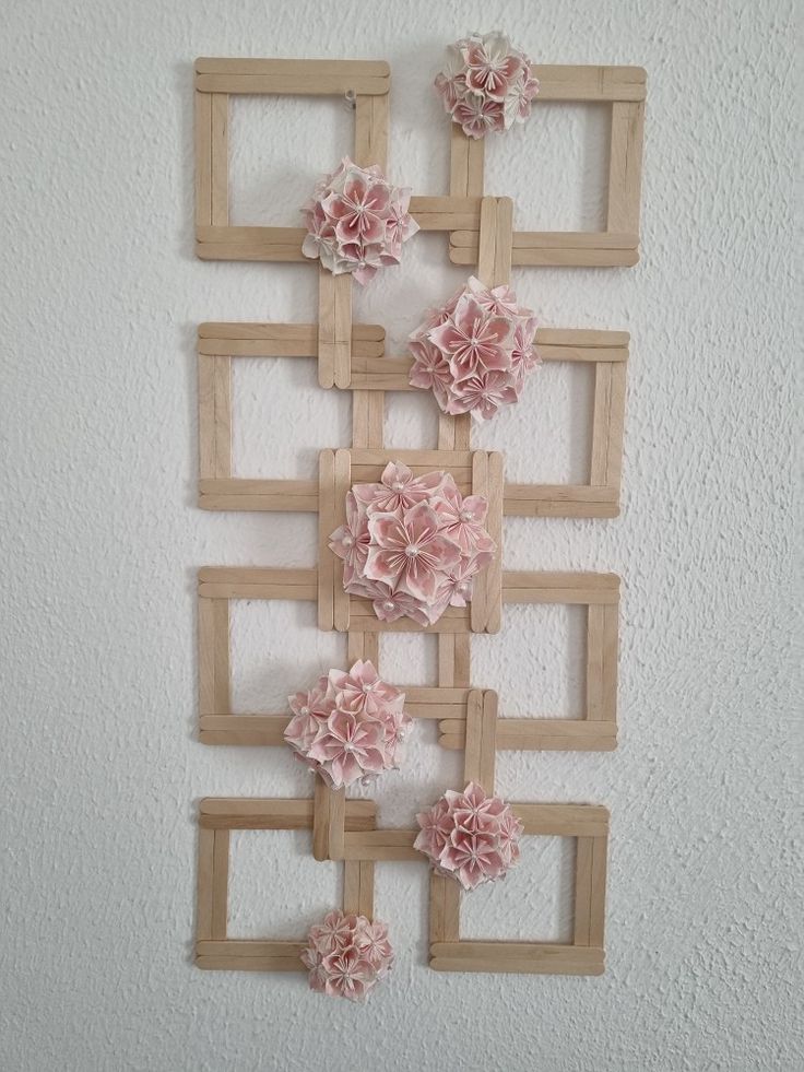 some pink flowers are hanging on the wall in front of a white wall with wooden frames