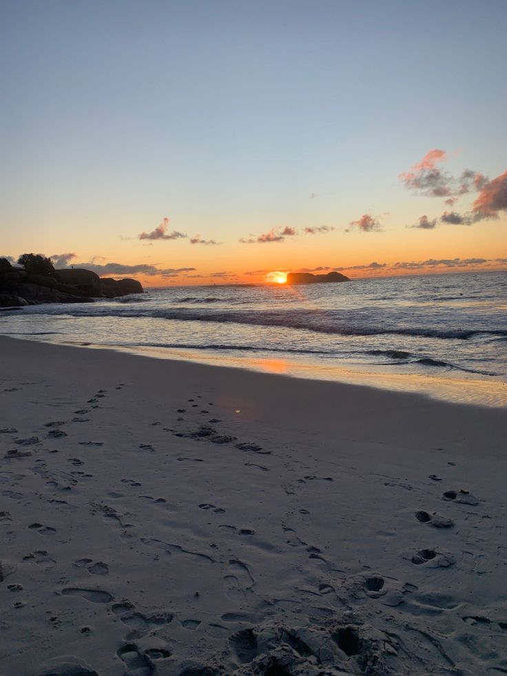 the sun is setting over the ocean with footprints in the sand and on the beach