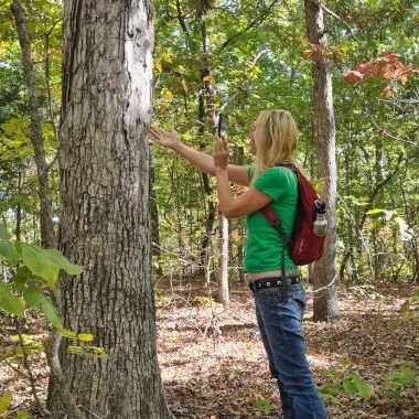 a woman standing next to a tree in the woods