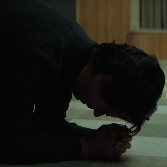 a man kneeling down on the floor praying with his hands clasped over his face and eyes closed