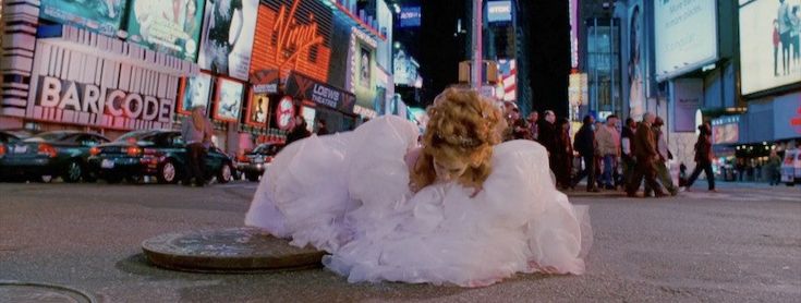 a woman in white dress sitting on the ground next to a street with billboards