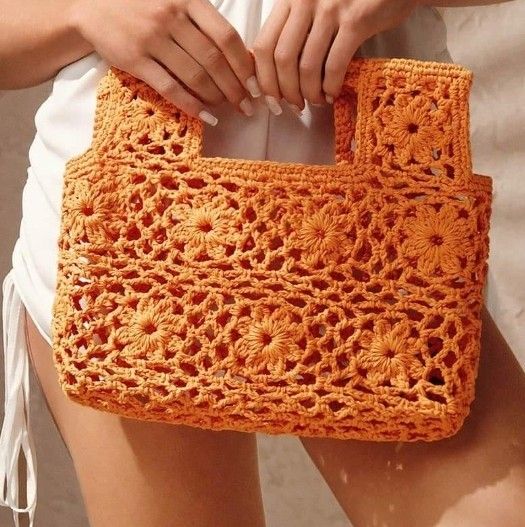 a crocheted orange purse being held by someone's hand with both hands