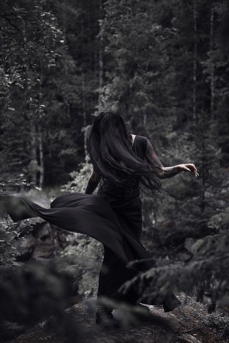 a woman with long hair is walking through the woods in black dress and flowing fabric