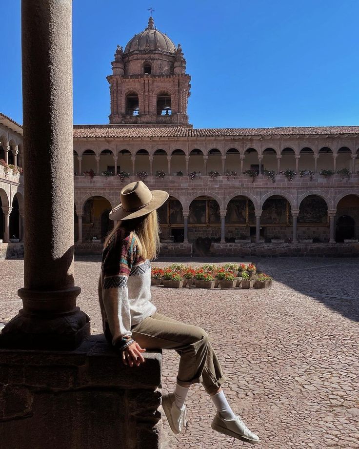 a woman sitting on top of a stone pillar in front of a building with a clock tower