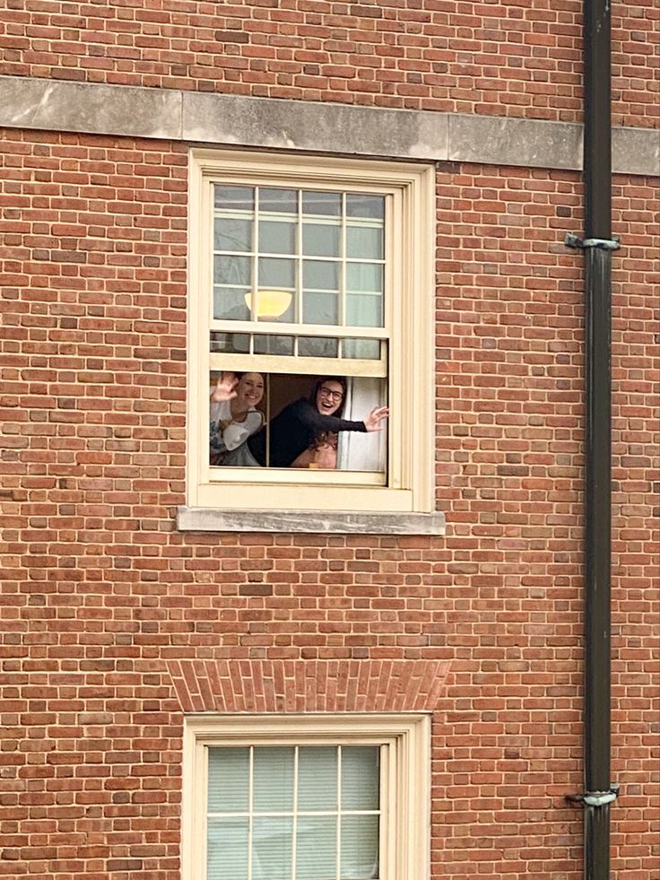 two people looking out the window of a brick building