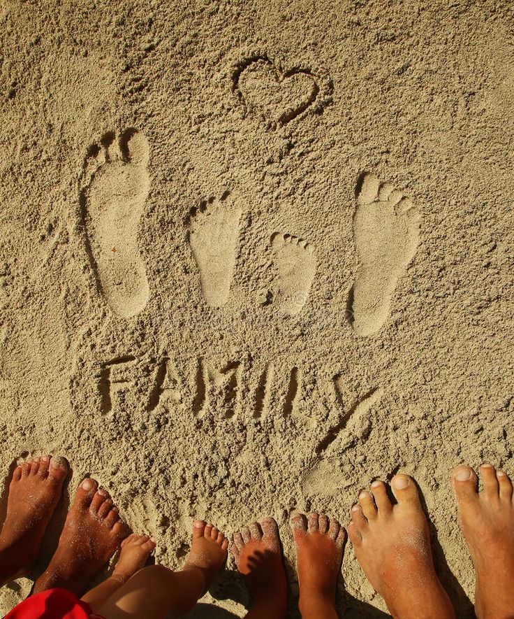 four people are standing in the sand with their feet up and one person has drawn a heart on it