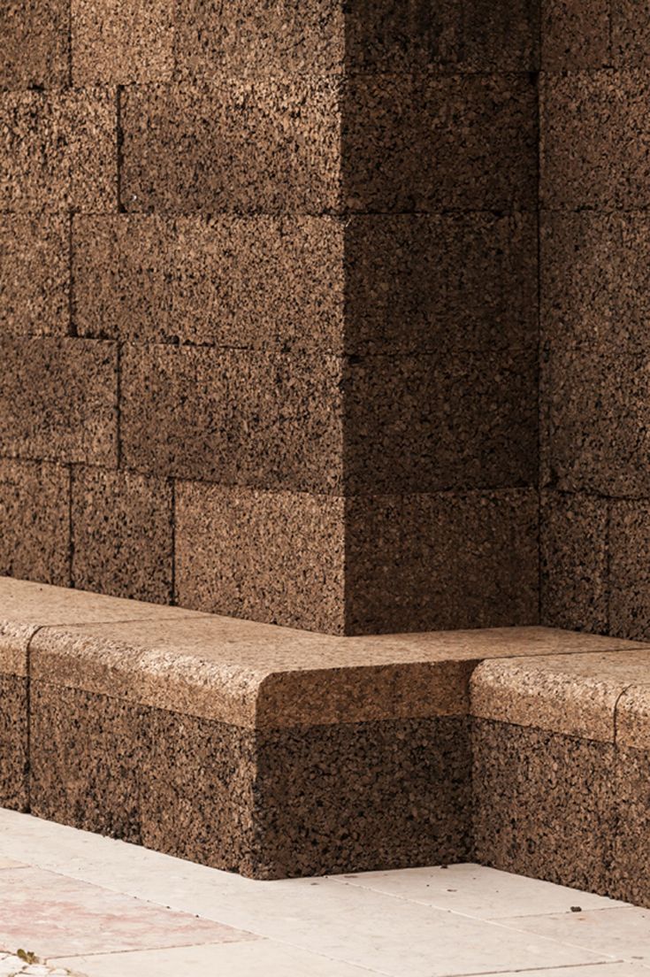 a stone bench sitting in front of a brick wall next to a cement block sidewalk