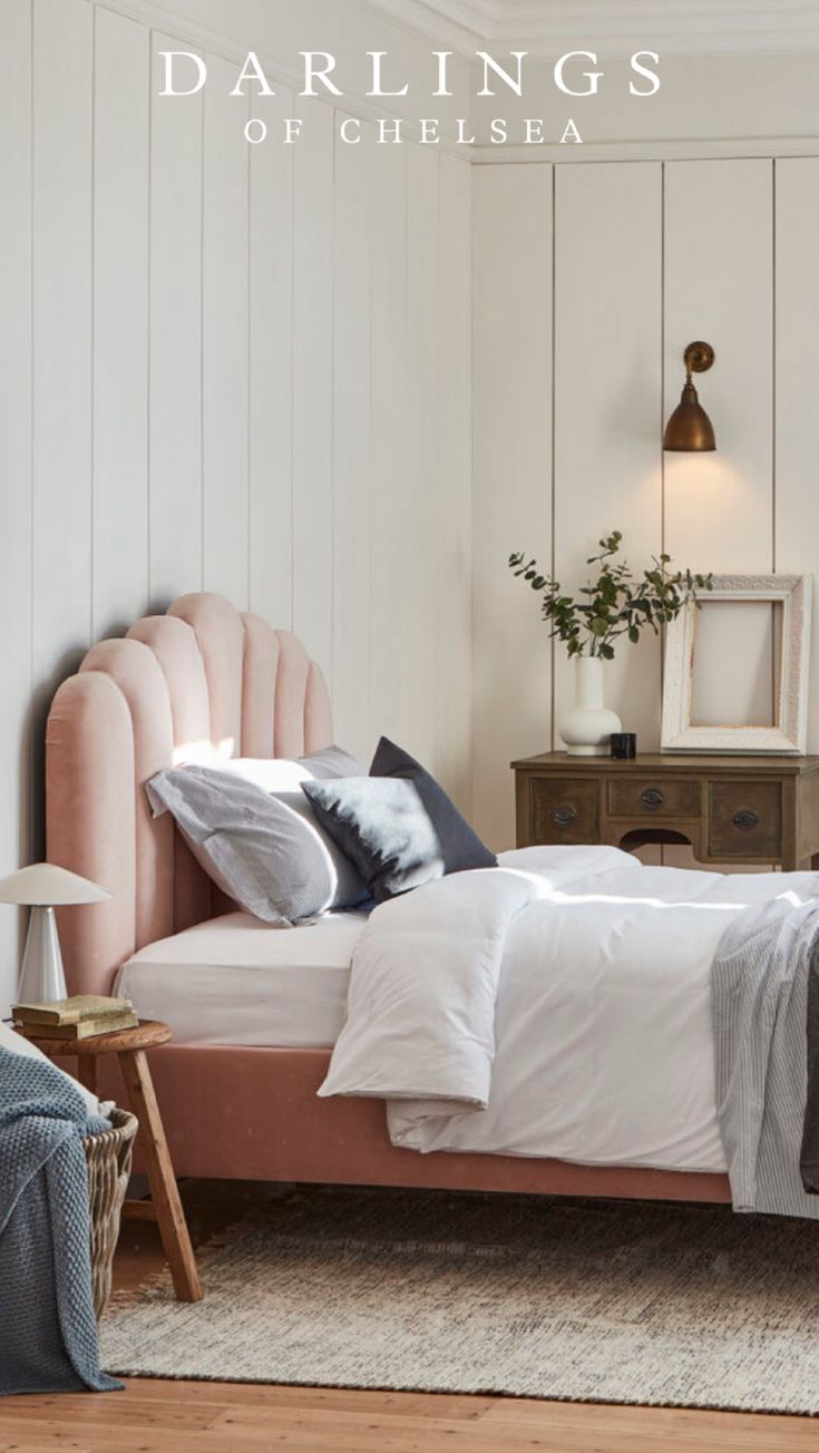 a bed with pink headboard and foot board in a white room next to a lamp