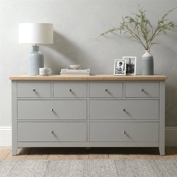 a grey dresser with two vases on top and a lamp in the corner next to it