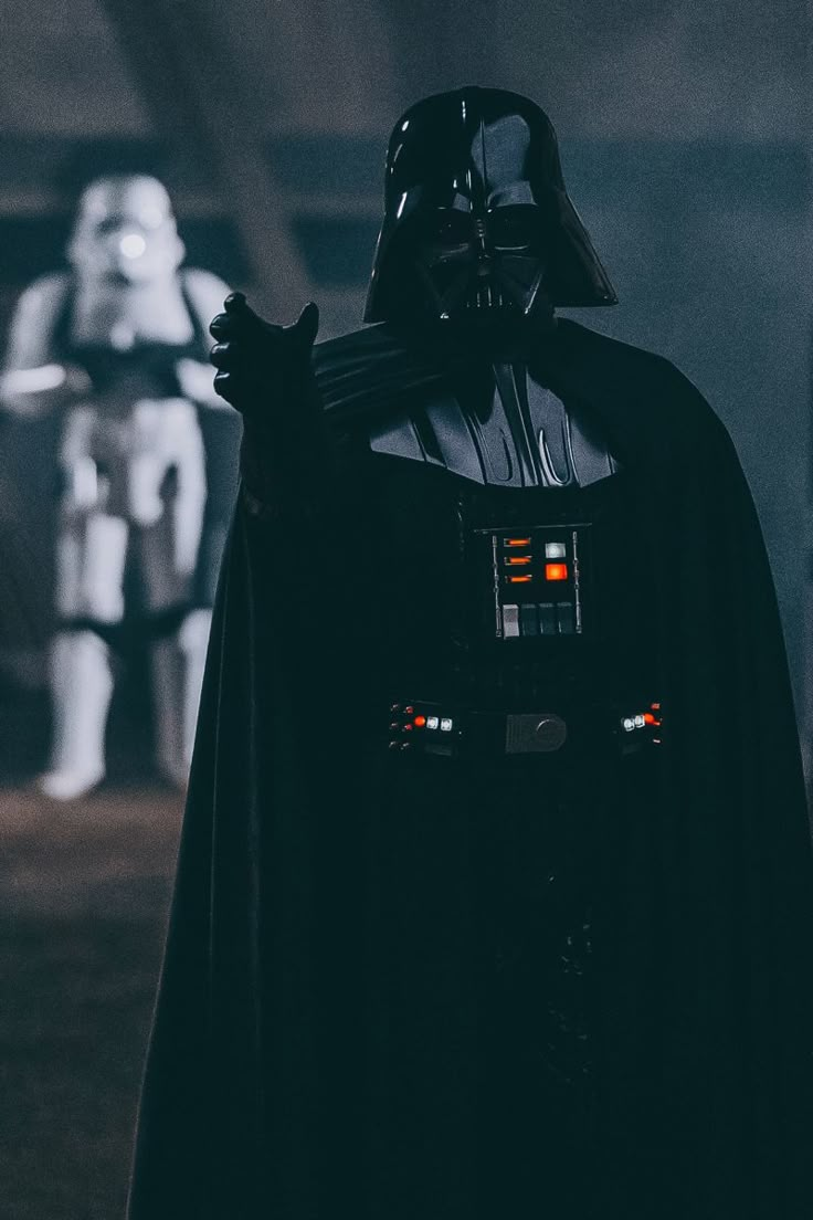 darth vader is standing in the dark with his lights on and other figures behind him