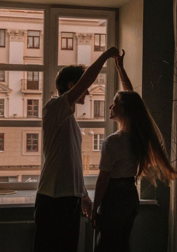 a man and woman standing next to each other in front of a window holding hands