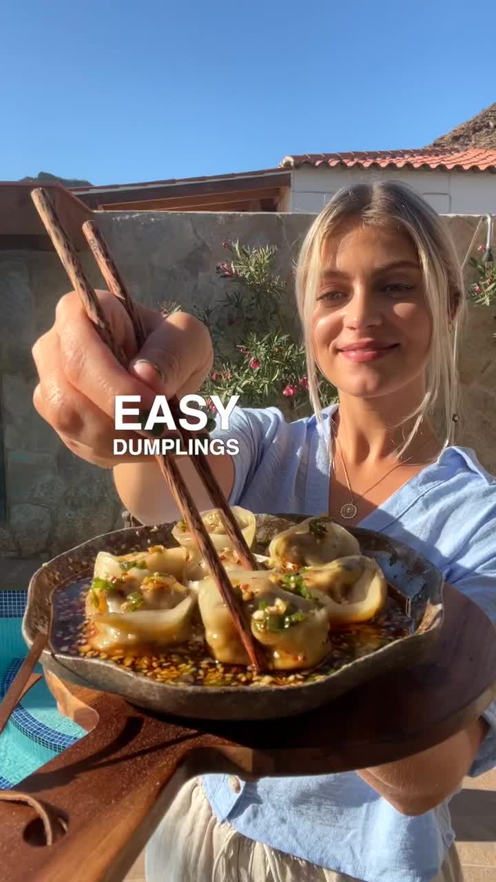 a woman holding a plate with dumplings in it and chopsticks sticking out