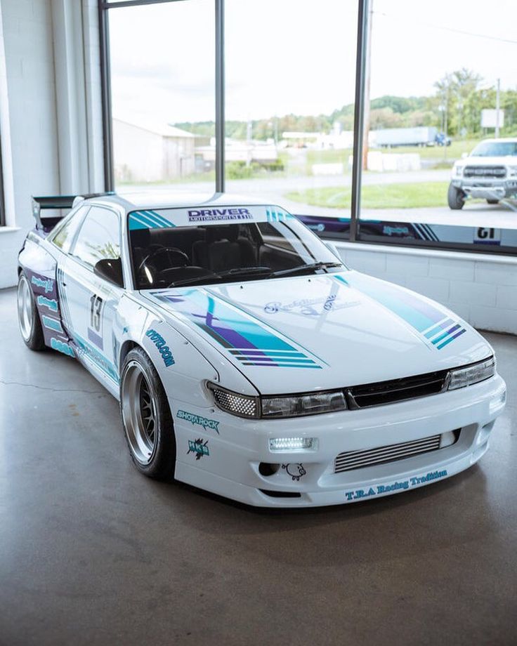 a white car parked inside of a building next to large windows with cars in the background