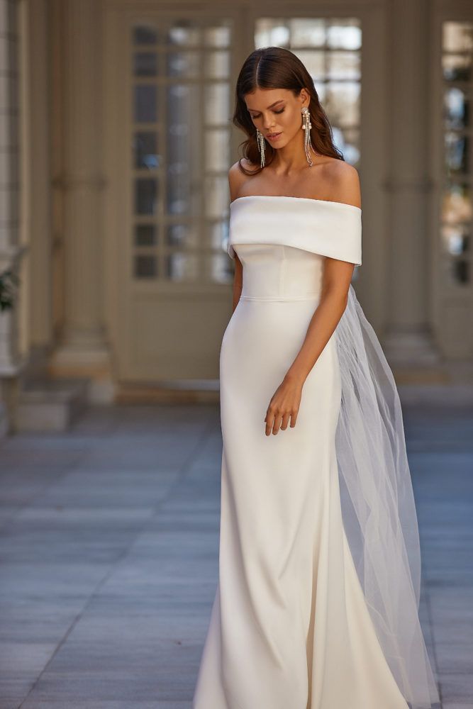 a woman in a white dress and veil posing for the camera with her hand on her hip