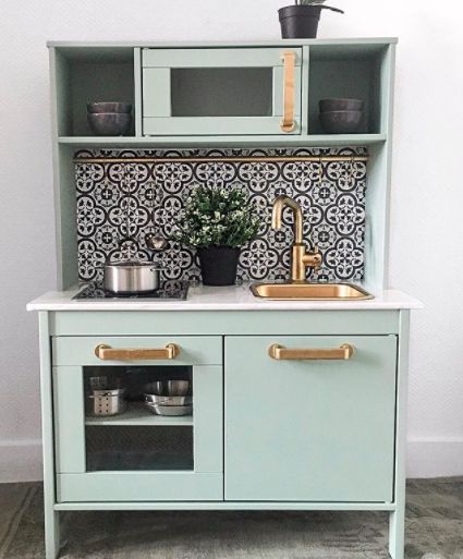 a small kitchen with green cabinets and white counter tops, gold pulls on the handles