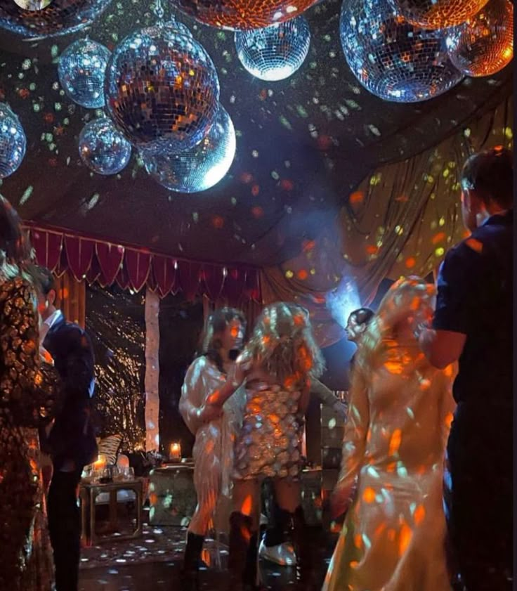 people are dancing at a party with disco balls hanging from the ceiling