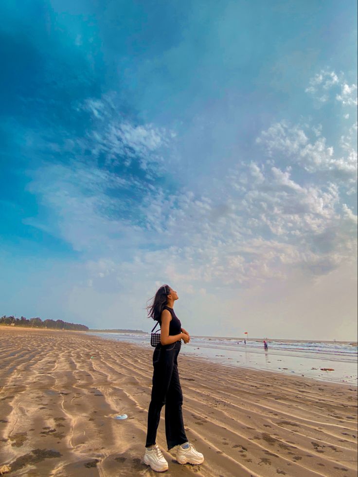 a woman standing on top of a sandy beach under a blue sky with white clouds