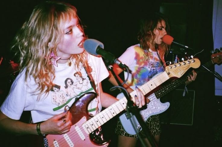 two young women playing guitars in front of microphones