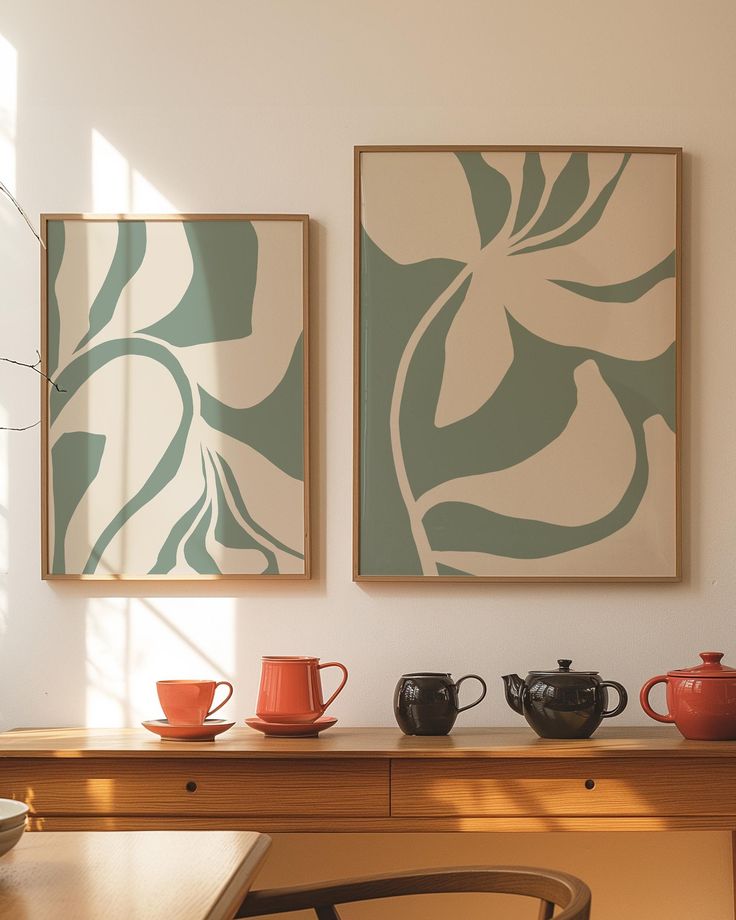 two paintings hanging on the wall above a table with cups and teapots in front of them