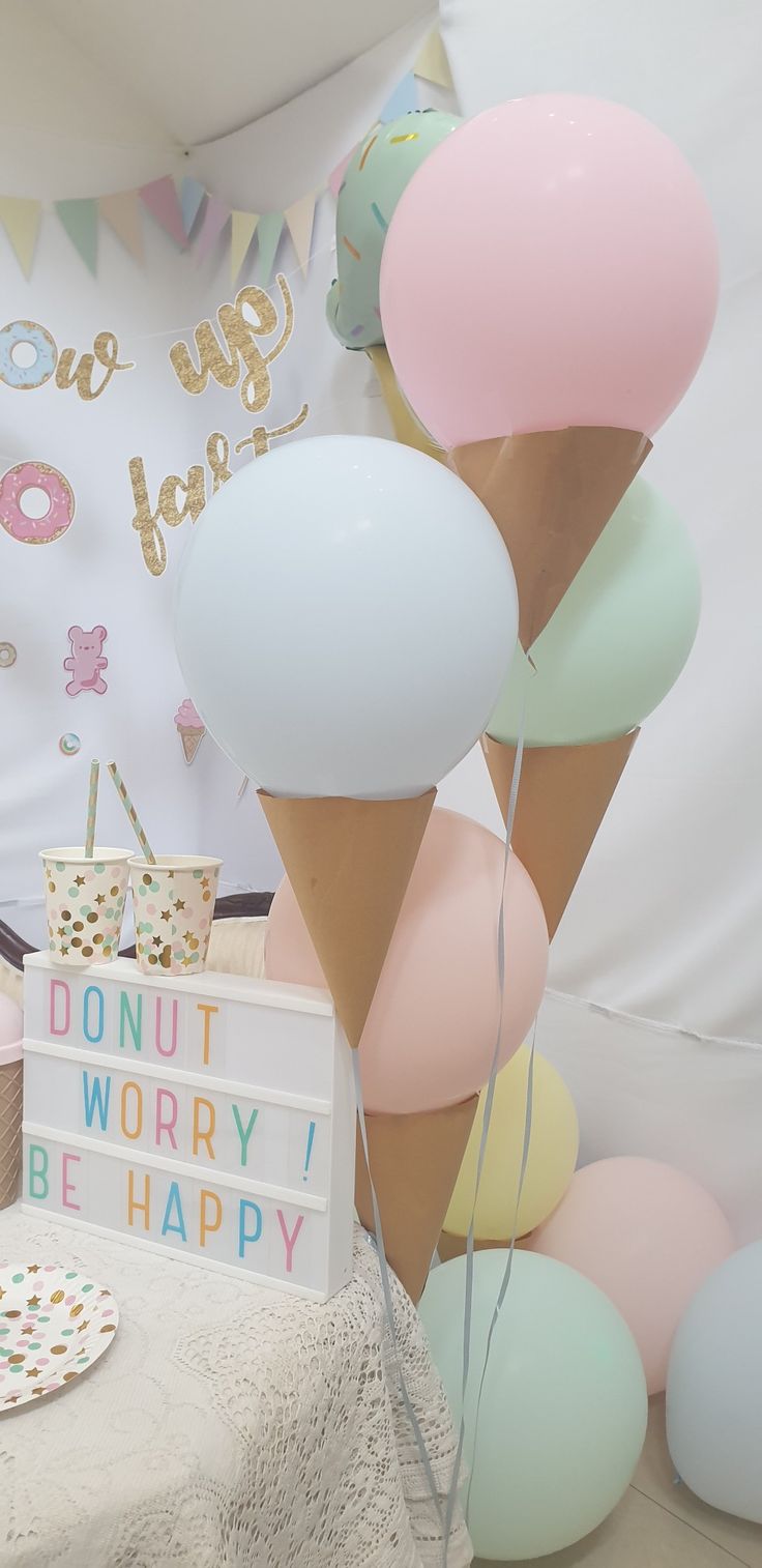 an ice cream cone and some balloons are on the table in front of a sign that says donut worry i be happy