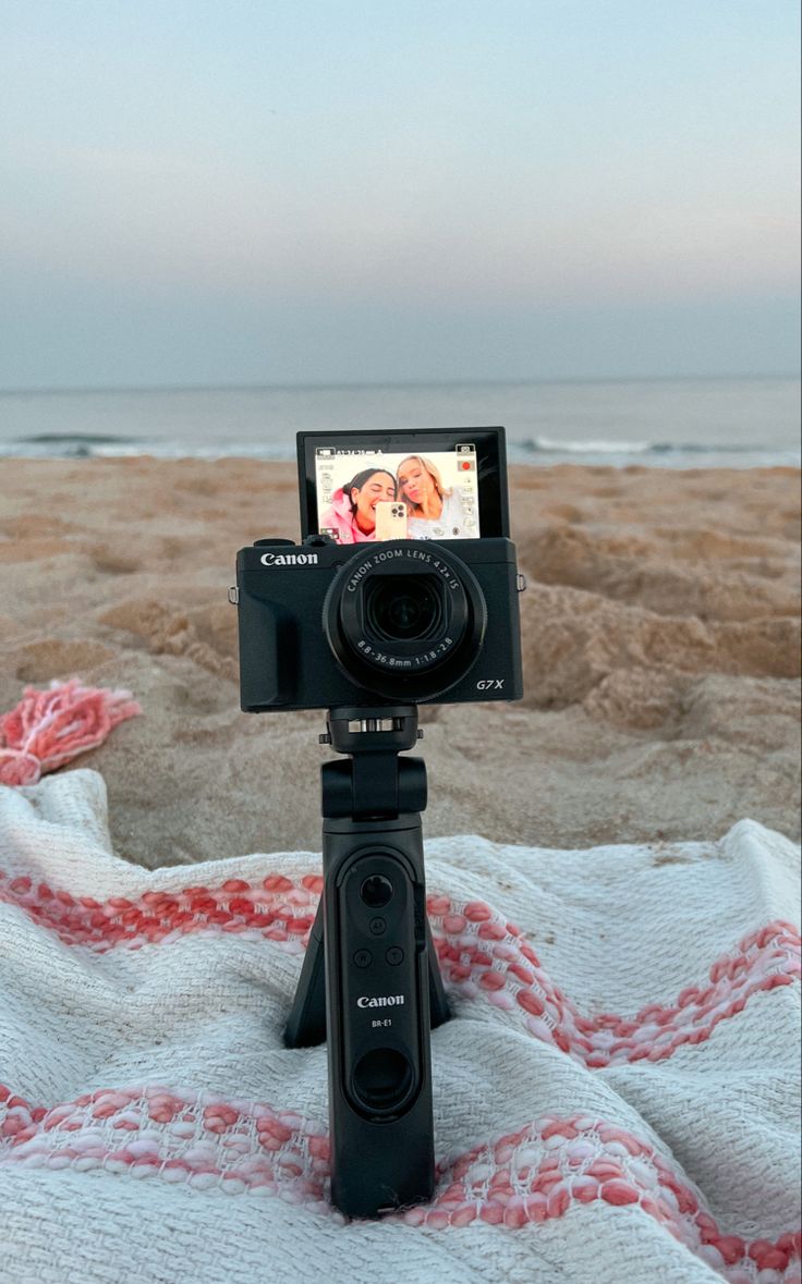 a camera sitting on top of a blanket next to the ocean with a beach in the background