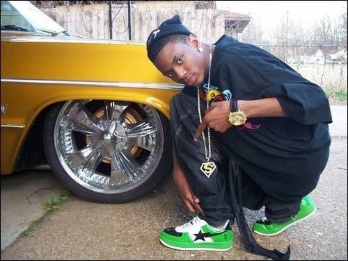 a young man kneeling next to a yellow car and wearing green converse shoes with his hand on the ground