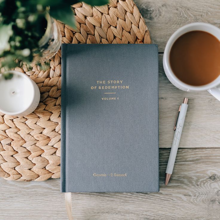 a book, pen and cup of coffee on a wicker place mat next to a basket