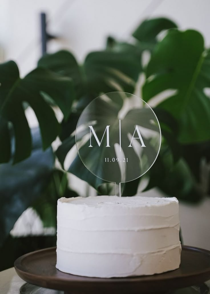 a white cake sitting on top of a wooden plate next to a green leafy plant