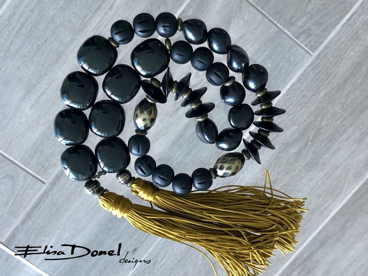 a tasseled necklace with black stones and gold beads on a white tile floor