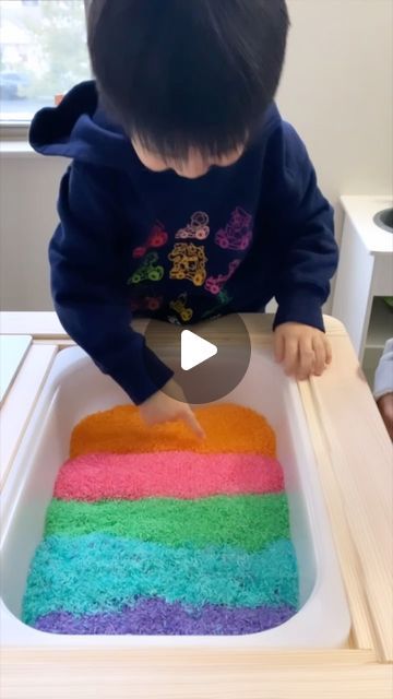 a toddler is playing with a rainbow cake