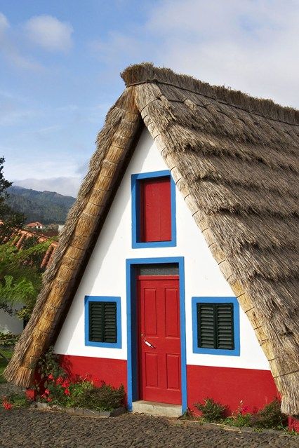 a white house with a thatched roof and red door surrounded by greenery on the hillside