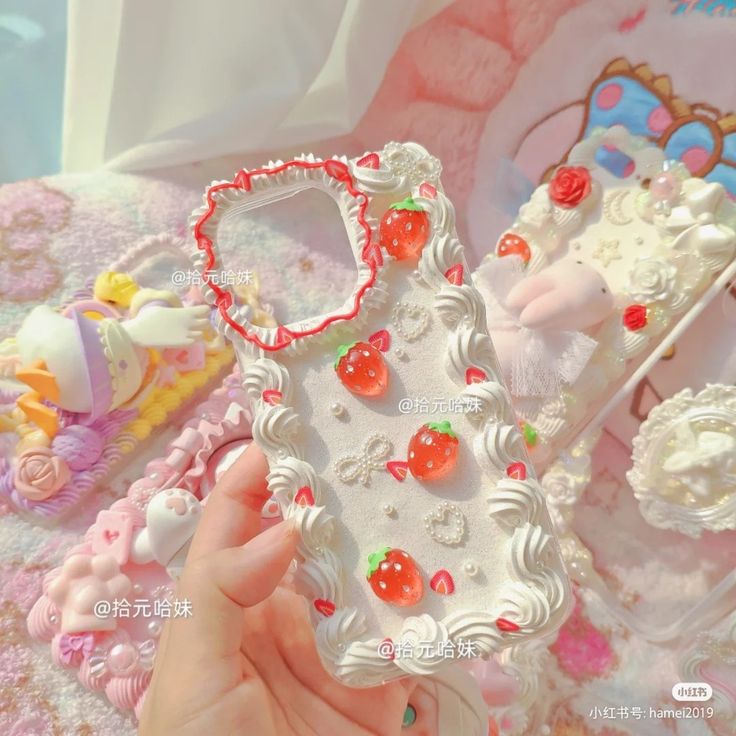 a hand holding a cell phone case made out of white frosted cake and cherries