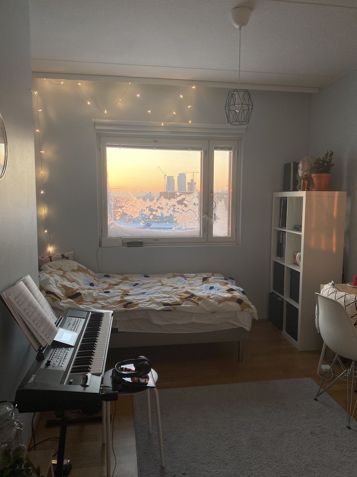 a bedroom with a bed, desk and piano in it's corner next to a window