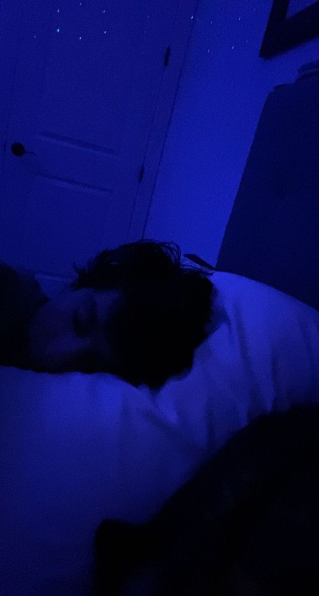 a person laying in bed with their head on the pillow at night under blue lights