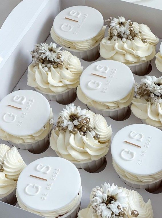 twelve cupcakes with white frosting decorated with flowers and leaves in a box