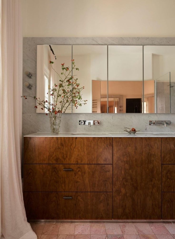 a bathroom with a double sink and large mirror on the wall, along with a vase filled with flowers