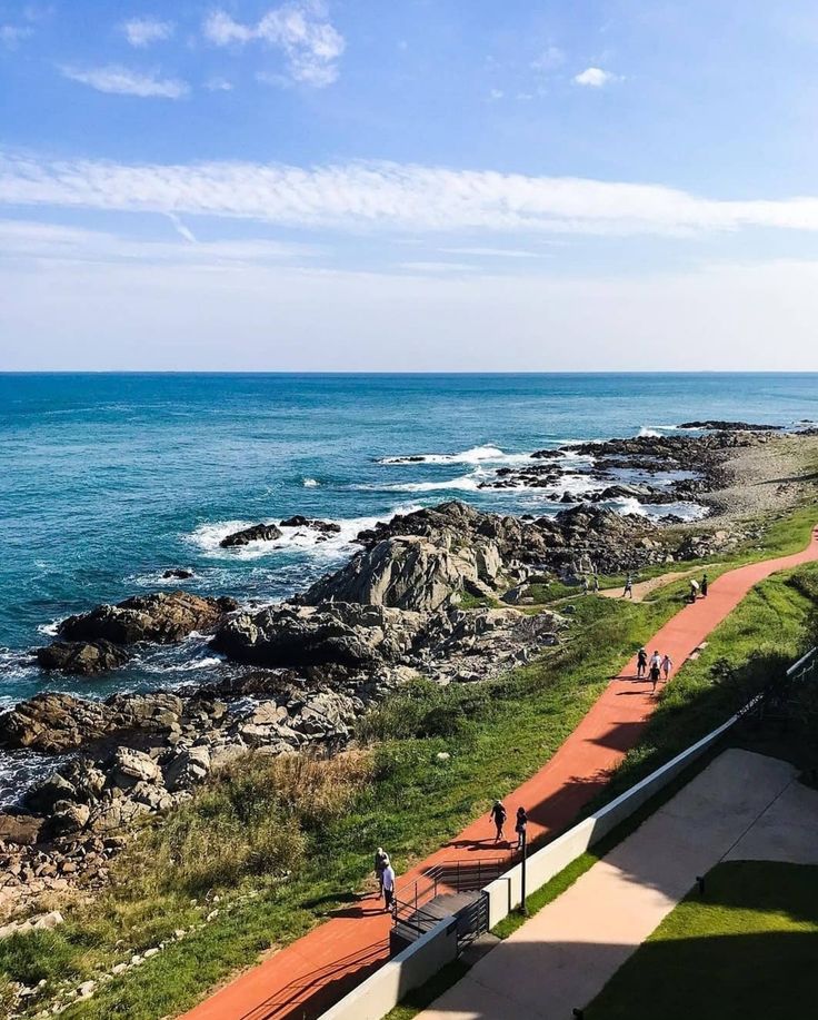 people are walking along the path by the ocean